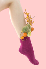 Woman's unshaven leg in dark pink socks on a pink background. Yellow flowers is in the socks.