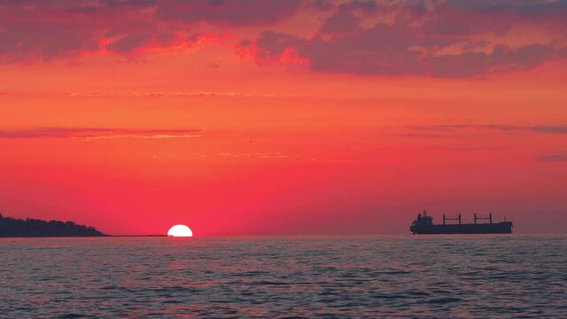 Sunrise with burning red sky over sea waves and industrial cargo ship
