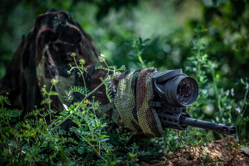 Sniper in camouflage suit in an ambush among the bushes. The shooter aims from a carbine with an optical sight.