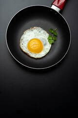 fried egg in black pan and parsley, on black background