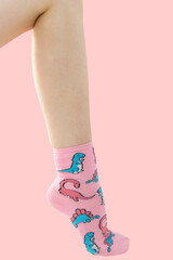 Woman's unshaven leg in pink socks with dinosaurs on a pink background. Pink flowers is in the socks.