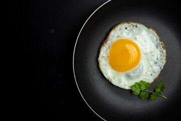 fried egg in black pan and parsley, on black background