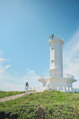 Fototapeta na wymiar A woman walking to the blue sky and white lighthouse of the resort. Jeju Island.