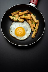 fried egg in black pan with french fries and parsley, on black background and slotted spoon and raw egg