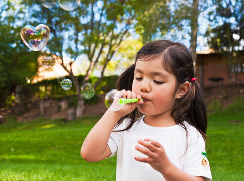 Little girl, blowing heart bubbles