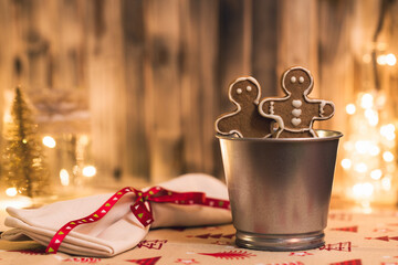 Christmas cute gingerbread men cookies in an iron bucket on the background of glowing garland and bokeh and rustic wooden boards. Creative, handmade.