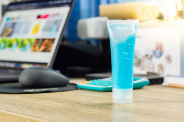 A select focus at tube of alcohol gel blue corona virus antiseptic is placed on the desk for hand clean. concept new normal now has a lap top (Note book) blur background.