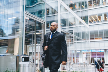 Formal serious executive man holding bag while walking in business center