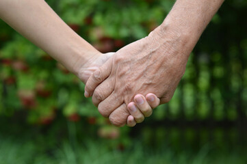 Granddaughter and grandmother holding hands outdoors close-up