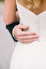 Groom hugs bride's waist. Hand with wedding ring close-up. Selective focus.