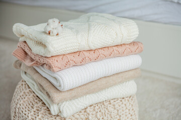 A stack of knitted sweaters, cotton. Women's sweaters lie on the ottoman. Cozy autumn clothes.