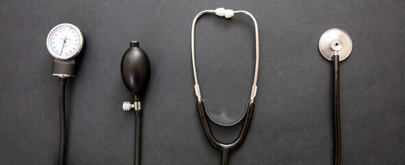 Medical stethoscope and sphygmomanometer on black background, top view.