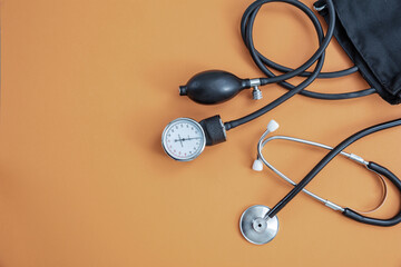 Medical stethoscope and sphygmomanometer on orange background, top view.