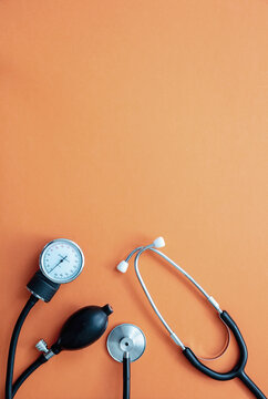 Medical stethoscope and sphygmomanometer on orange background, top view.