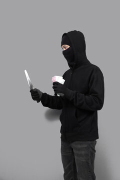 Burglar concept,money and a knife in the hands of a bandit on gray background