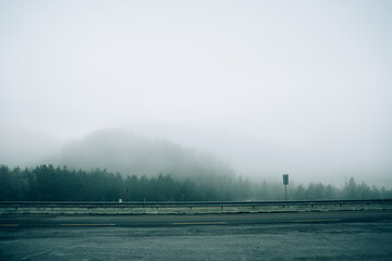 Naklejka na ściany i meble Creepy empty road on background of misty dense forest on hills