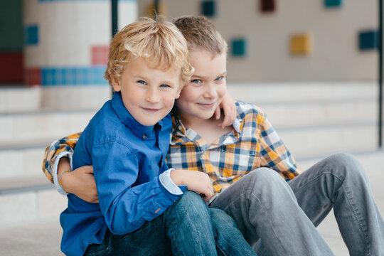 Two happy brothers sitting on the front steps of a school looking at camera