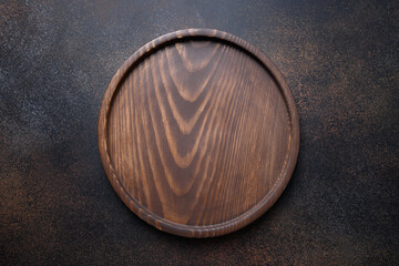 Wooden round cutting board or tray on dark brown kitchen background. Space for design. Top view,...