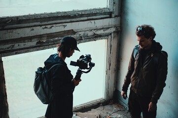 Long haired operator filming curly guy in destroyed building at window