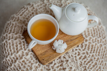 A mug of hot tea, a teapot, a wooden stand on an ottoman. Cozy autumn. Winter breakfast. Cotton.