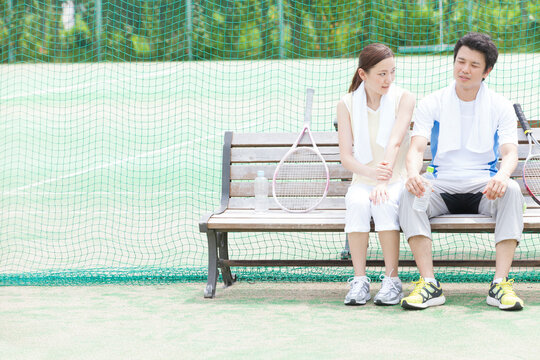 テニスコートのベンチで休憩するカップル
