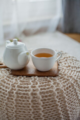 Fototapeta na wymiar A mug of hot tea, a teapot, a wooden stand on an ottoman. Cozy autumn. Winter breakfast. Cotton.