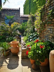Fototapeta premium Widok na patio ze śródziemnomorską roślinnością. Akcenty w stylu prowansalskim. Ceglasty mur otoczony zielenią.