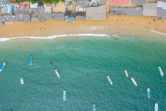 Vista a&eacute;rea cenital sobre la playa de la bah&iacute;a de Puerto Marqu&eacute;s en Acapulco, Guerrero. Se observa los tradicionales techos de palma de los comercios y algunas barcas sobre el mar.