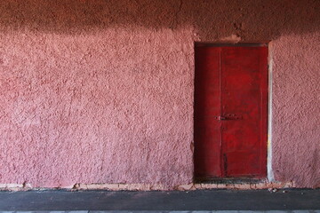 Locked old massive red-brown metal double-leaf door in the doorway of a pink wall with a rough coarse plaster texture