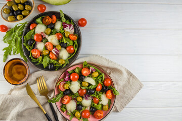 Two servings of salad with melon, tomatoes and olives on a white wooden background. Free space for the text.