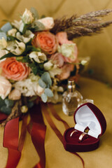 Wedding bridal bouquet of roses and eucalyptus branches next to a box of wedding rings on yellow velvet. Wedding and love concept