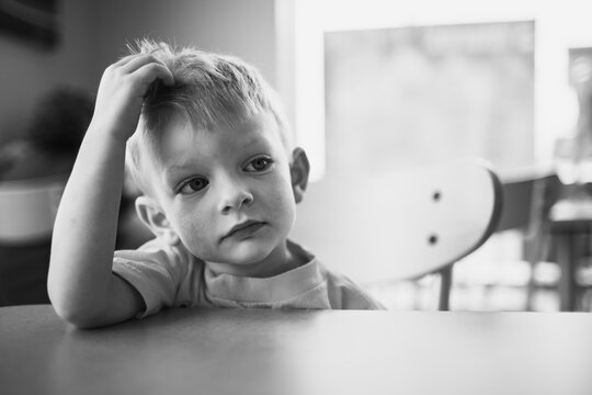 a little boy sitting at an empty table looking grumpy