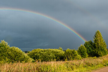 Naklejka premium Landscape. Weather specific. Double colorful rainbow in dramatic sky after the rain.