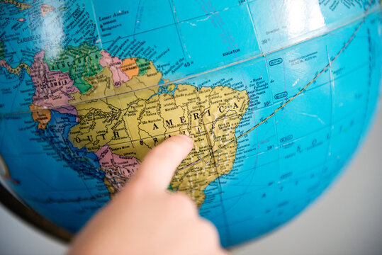 Child points to the country of Brazil on an old school globe