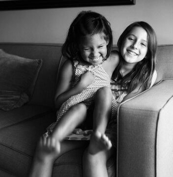 Two multiethnic girls giggling on couch in black and white