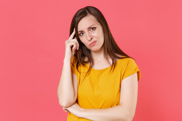 Worried perplexed displeased puzzled young brunette woman 20s wearing yellow casual t-shirt posing standing looking camera put hand on head isolated on pink color wall background studio portrait.