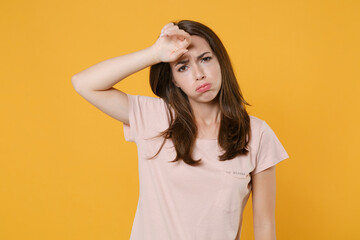 Exhausted tired displeased young brunette woman wearing pastel pink casual t-shirt standing posing put hand on head looking camera isolated on bright yellow color wall background studio portrait.