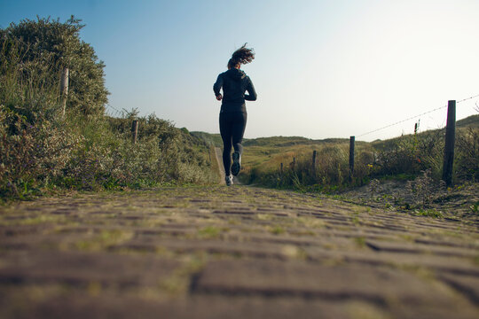 Young woman running over a path through the dunes during her workout.