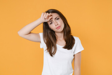 Exhausted tired upset confused young brunette woman 20s wearing white blank empty design casual t-shirt posing standing put hand on head looking camera isolated on yellow background studio portrait.