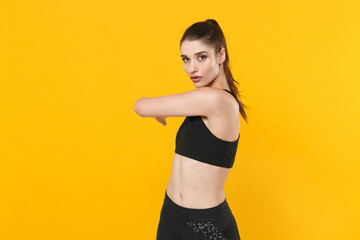 Fototapeta na wymiar Attractive young fitness sporty woman 20s wearing black sportswear posing working out training doing stretching exercising looking camera isolated on bright yellow color background studio portrait.