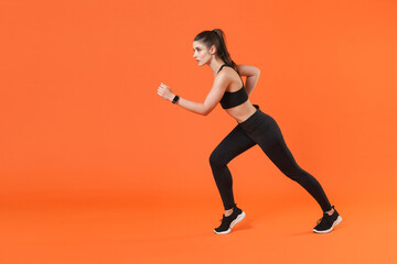 Fototapeta na wymiar Full length side view portrait of attractive strong young fitness sporty woman 20s wearing black sportswear training working out running looking aside isolated on orange color wall background studio.