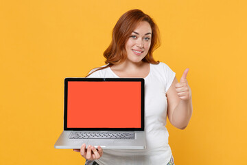 Smiling redhead plus size body positive female woman in white t-shirt hold laptop pc computer with blank empty screen mock up copy space showing thumb up isolated on yellow background studio portrait.