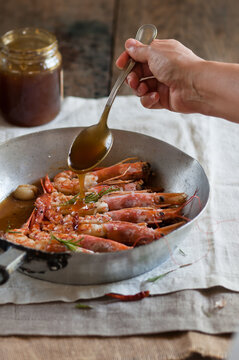 prawns in a pan with a hand pouring a tablespoon of honey