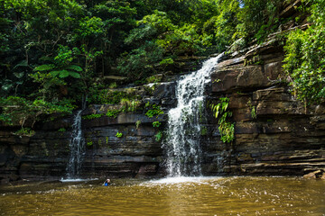 A man, swimming under tropical waterfall