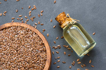 Heap of Flax seeds or linseeds in spoon or bowl with glass of flax seed oil on rustic backdrop....