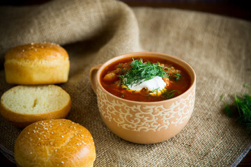 hot beetroot soup with sour cream, herbs and rolls in a ceramic bowl