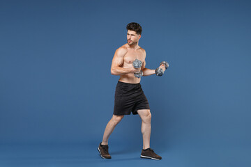 Fototapeta na wymiar Full length portrait of young bearded fitness sporty strong guy bare-chested muscular sportsman isolated on blue background. Workout sport motivation lifestyle concept. Doing exercise with dumbbells.