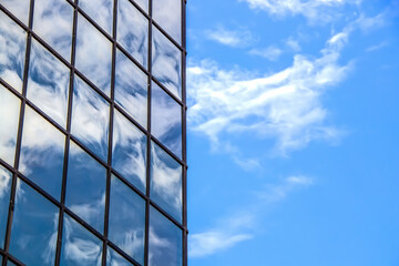 Blue cloudy sky reflected by mirror panes in modern building making an abstract image - room for copy