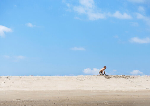 Boy plays in the sand on a beach under a blue sky