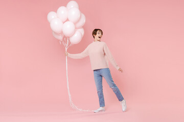 Full length portrait side view of excited young woman in casual sweater isolated on pastel pink background. Birthday holiday party people emotions concept. Celebrating hold air balloons looking aside.